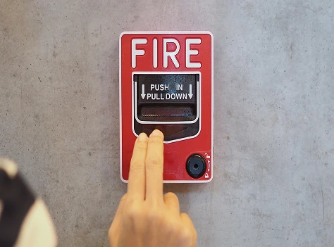 Hand activating a red fire alarm pull station mounted on a wall