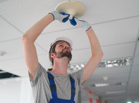 Technician installing a ceiling-mounted smoke detector in a commercial building